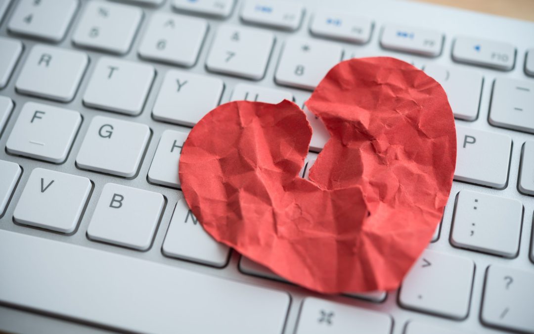Red broken heart paper on white keyboard computer background. Online internet romance scam or swindler in website application dating concept. Love is bait or victim.
